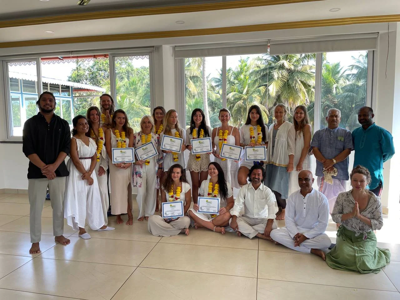 A group of students dressed in white or light-colored clothing holding 300 Hours YTTC certificates in Mysore at Rishikul Yogshala
