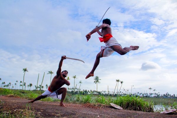 Kalaripayattu students performing an intense sword fight with aerial moves in a scenic outdoor setting