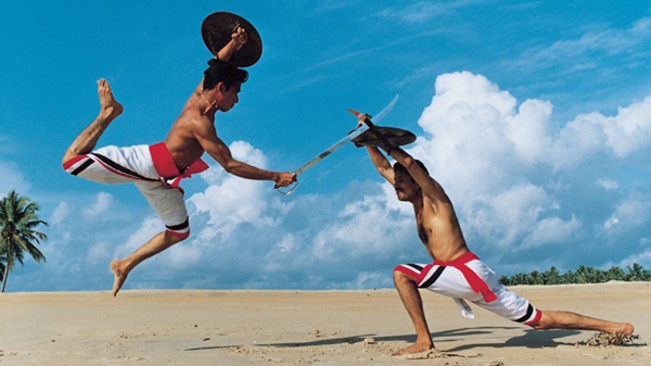 Two Rishikul Yogshala students practicing Kalaripayattu with sword and shield on a sandy beach