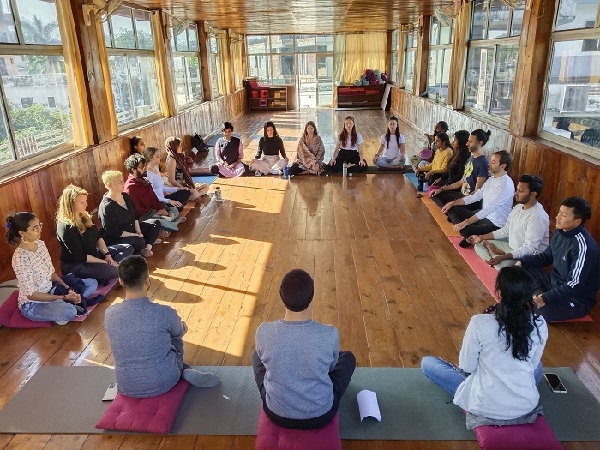 Yoga students in a group discussion – A peaceful gathering in a sunlit wooden hall for mindfulness and learning