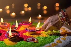 Diwali Celebration with Diyas at Rishikul Yogshala Hand lighting a diya on a colorful rangoli during Diwali celebrations